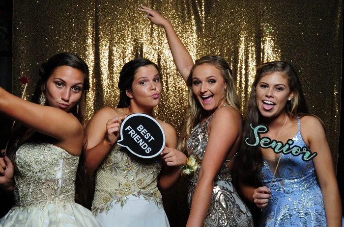 Four friends posing with props in front of a gold backdrop at prom